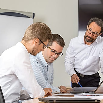 Drei Männer mit Brille an einem Konferenztisch