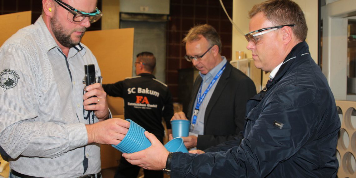 Ein blauer Topf bringt den Kreislauf in Schwung: Produktionsleiter Ulrich Lampe (links) erläuterte dem Lohner Bürgermeister Tobias Gerdesmeyer (rechts) im Rahmen der XXL-Werksführung, die Herstellung des neuen Reycling-Produktes. Bild: Pöppelmann