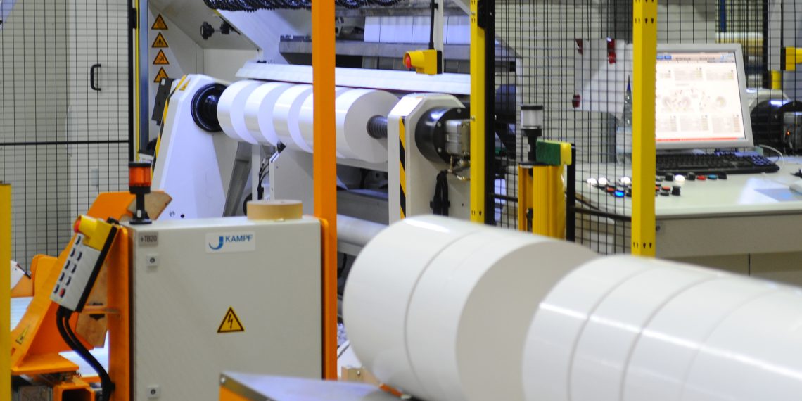 „Ich bin eine Rolle – holt mich hier raus“: Automatisierte Förderfahrzeuge vor einer Schneidanlage, auf der Haftmaterial kundenspezifisch konfektioniert wird. Bei HERMA kommunizieren 14 unterschiedliche Anlagen miteinander, um aktionsgesteuerte Fertigungsprozesse zu ermöglichen. Bild: Herma