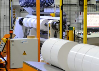 „Ich bin eine Rolle – holt mich hier raus“: Automatisierte Förderfahrzeuge vor einer Schneidanlage, auf der Haftmaterial kundenspezifisch konfektioniert wird. Bei HERMA kommunizieren 14 unterschiedliche Anlagen miteinander, um aktionsgesteuerte Fertigungsprozesse zu ermöglichen. Bild: Herma